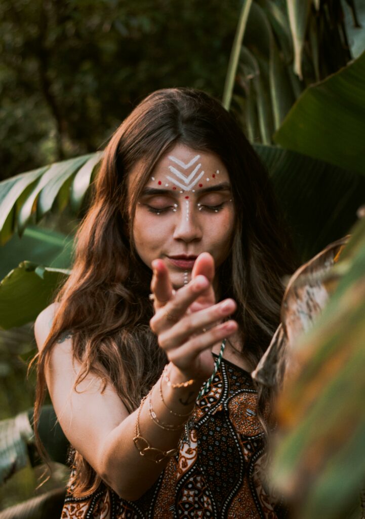 Portrait of a young woman with tribal-inspired makeup surrounded by lush tropical foliage.