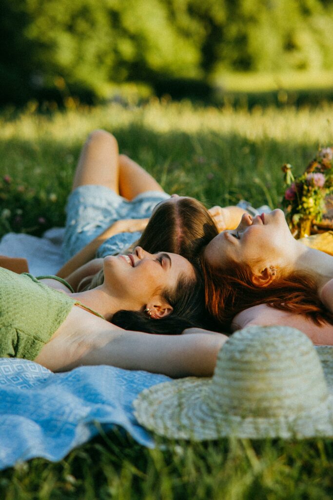 Three women enjoying a sunny day on a picnic blanket in the park, embracing togetherness and nature.