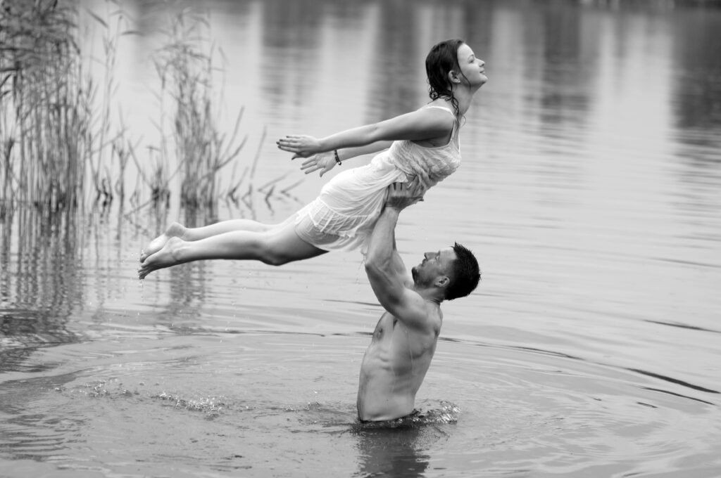 Black and white photo of a couple in a romantic pose with a man lifting a woman in water.