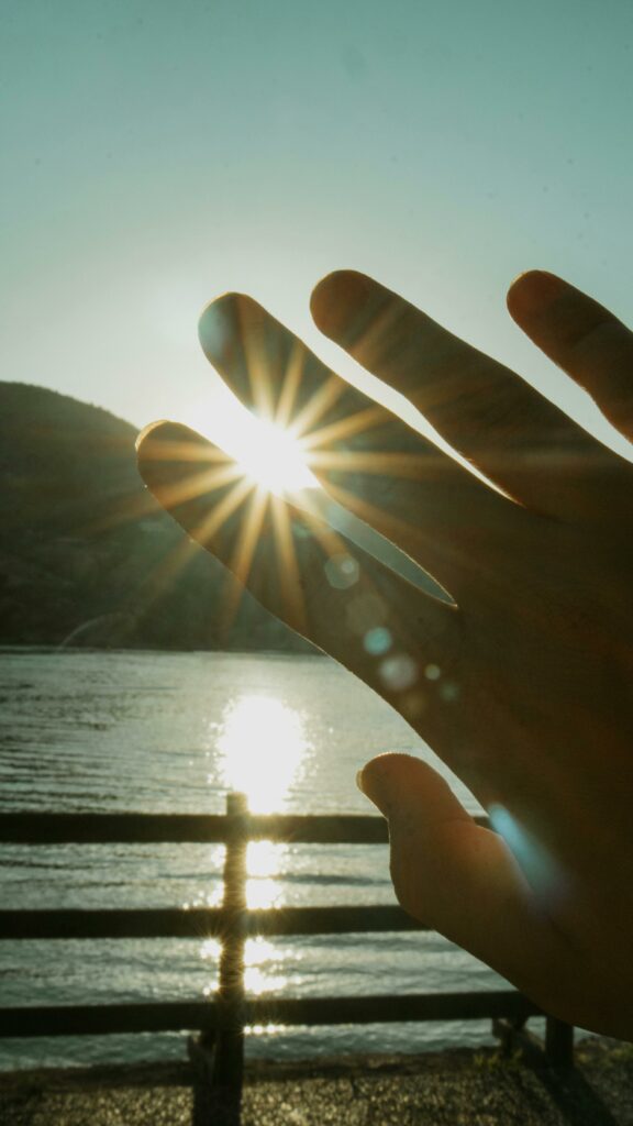 A hand silhouette capturing sunrays and reflections by a serene lake, evoking tranquility.
