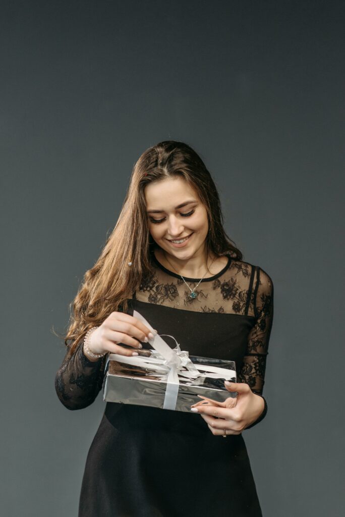 Smiling woman in elegant black dress opening a gift with a white ribbon.