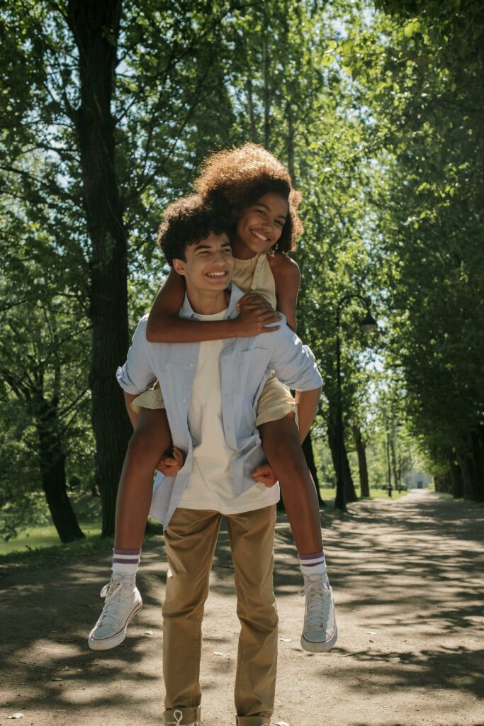 A cheerful couple of teenagers enjoying a playful moment in a sunny park.
